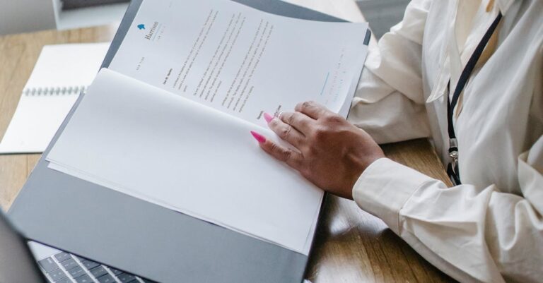 From above side view of crop African American female manager reading report of project while working with laptop in office